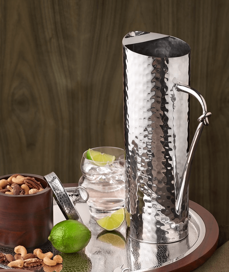 A stainless steel water pitcher on a tray