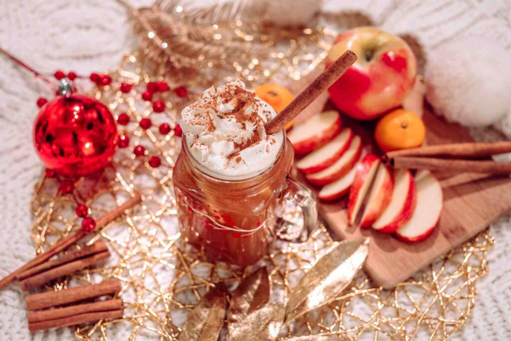 Apple cider with whipped cream surrounded by apple slices and cinnamon sticks