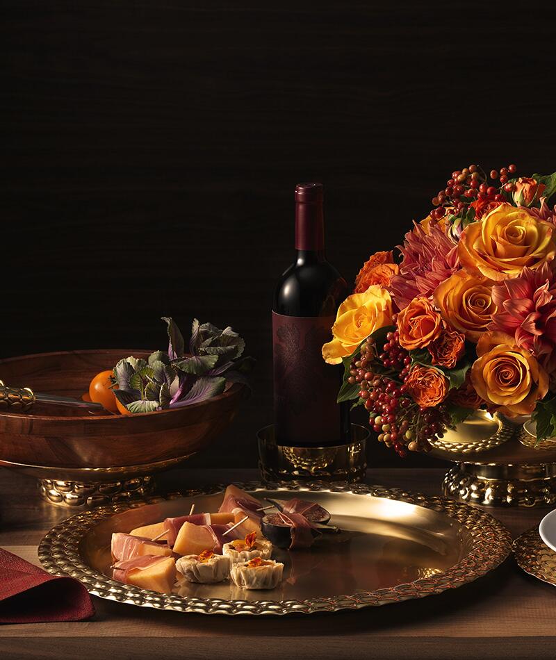 An ornate table with flowers, wine, and serveware from the Helios collection