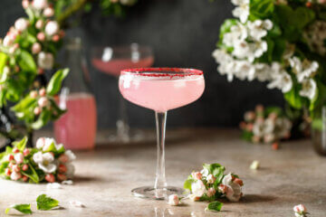A pink cocktail drink surrounded by apple blossom